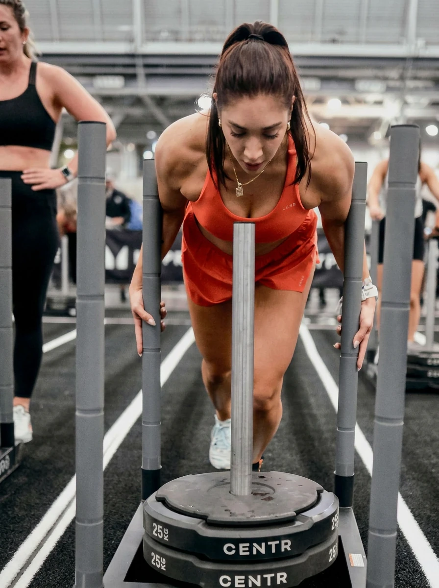 Madison Gold competing at a HYROX race, pushing through a sled workout station